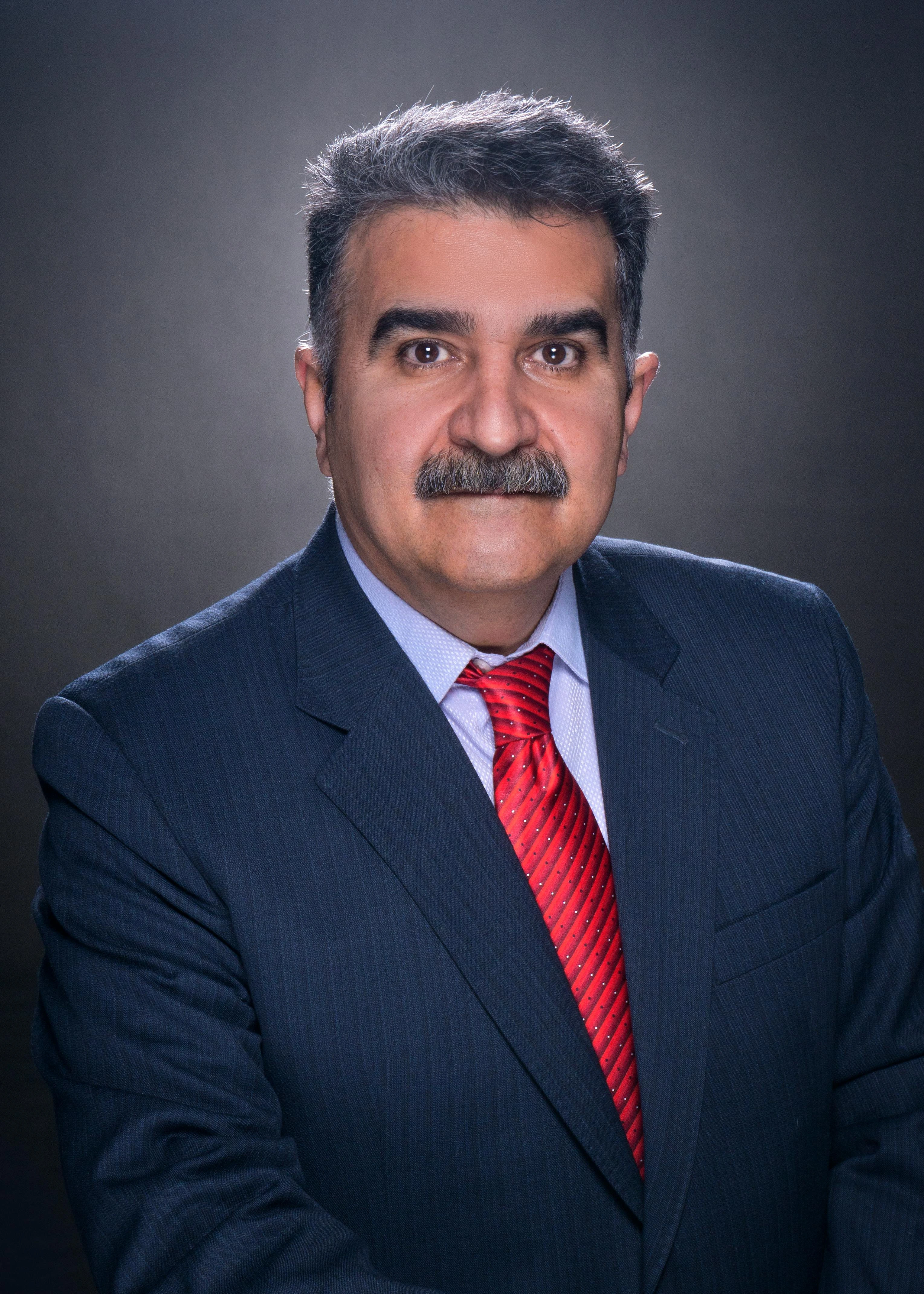 Photograph of a professional man with long hair and glasses in a suit in an office setting.